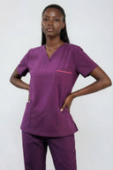 Model wearing Plum Purple ST247 Scrub Top in a studio setting, three-quarter view