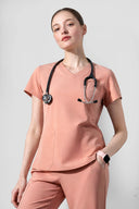 Model wearing Coral Peach CST203 Scrub Top in a studio setting, three-quarter view