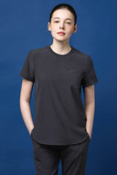 Model wearing Grey CST201 Scrub Top in three-quarter view with blue studio background