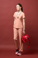 Model wearing Coral Peach CST203 Scrub Top by Good Uniform holding medical gears, full front view