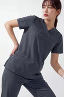Model wearing Cool Grey ST215 Scrub Top in a studio setting, three-quarter view