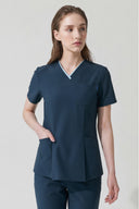 Model wearing Antique Blue Anyone Zip Scrub Top in a clinical setting, three-quarter view