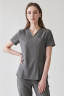 Model wearing Mild Grey Anyone Zip Scrub Top in a studio setting, three-quarter view