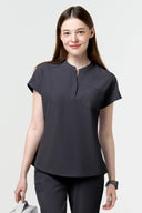 Model wearing Grey CST202 Scrub Top in a clinical setting, three-quarter view