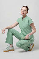 Model wearing Smoke Mint CST202 Scrub Top by Good Uniform, full side view sitting down