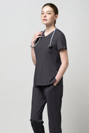 Model wearing Grey CST203 Scrub Top in a studio setting, three-quarter view from the side