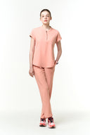 Model wearing Coral Peach CST202 Scrub Top by Good Uniform, full front view in an off-white studio setting