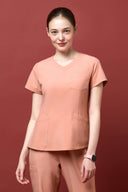 Model wearing Coral Peach CST203 Scrub Top in a studio setting, three-quarter view from the front