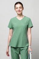 Model wearing Smoke Mint CST203 Scrub Top in a studio setting, three-quarter view holding a textbook.