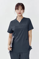 Model wearing Cool Grey ST215 Scrub Top in a clinical setting, three-quarter view