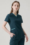 Model wearing Antique Blue Anyone Zip Scrub Top in a studio setting, three-quarter view