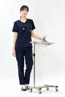 Model wearing Stellar Navy ST002 Scrub Top by Good Uniform in a clinical setting, full front view