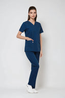 Model wearing Matte Blue Avison Scrub Top by Good Uniform with hand in the pocket, full front view
