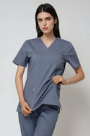 Model wearing Mist Grey Avison Scrub Top showing stretchability of the scrub, three-quarter view