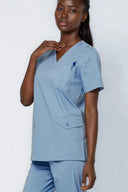 Model wearing Soft Blue Avison Scrub Top in a stdio setting, three-quarter view slightly from the side