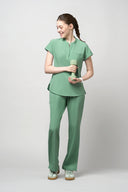 Model wearing Smoke Mint CST202 Scrub Top by Good Uniform, full front view holding an item
