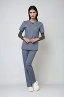 Model wearing Mist Grey Avison Scrub Top by Good Uniform, full front view in a studio setting