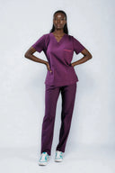 Model wearing Plum Purple ST247 Scrub Top by Good Uniform, full front view with arms resting on the waist