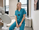 Dental professional in teal scrubs sitting in a dental office.